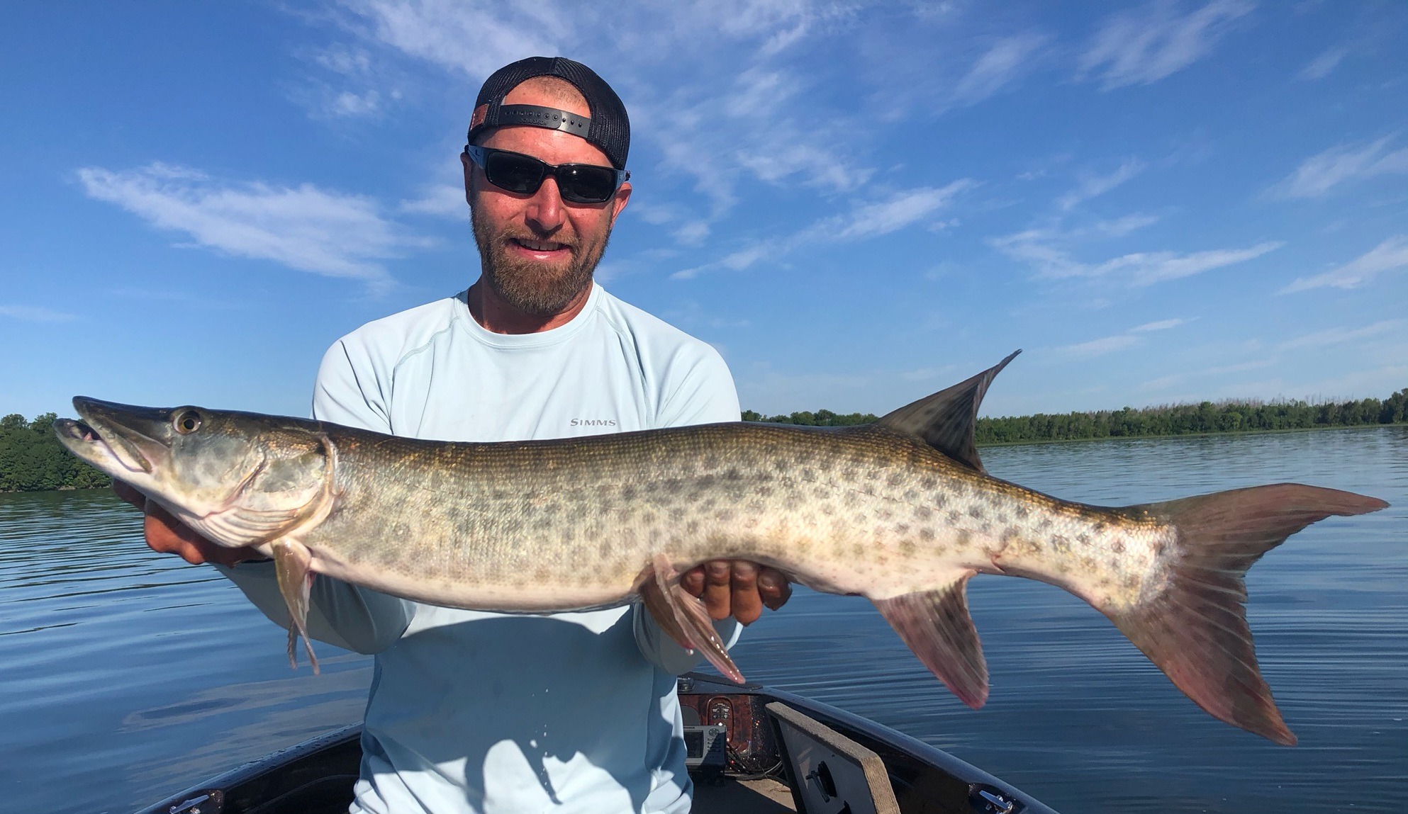A man with a backwards baseball cap holds a huge fish he just caught on a guided trip